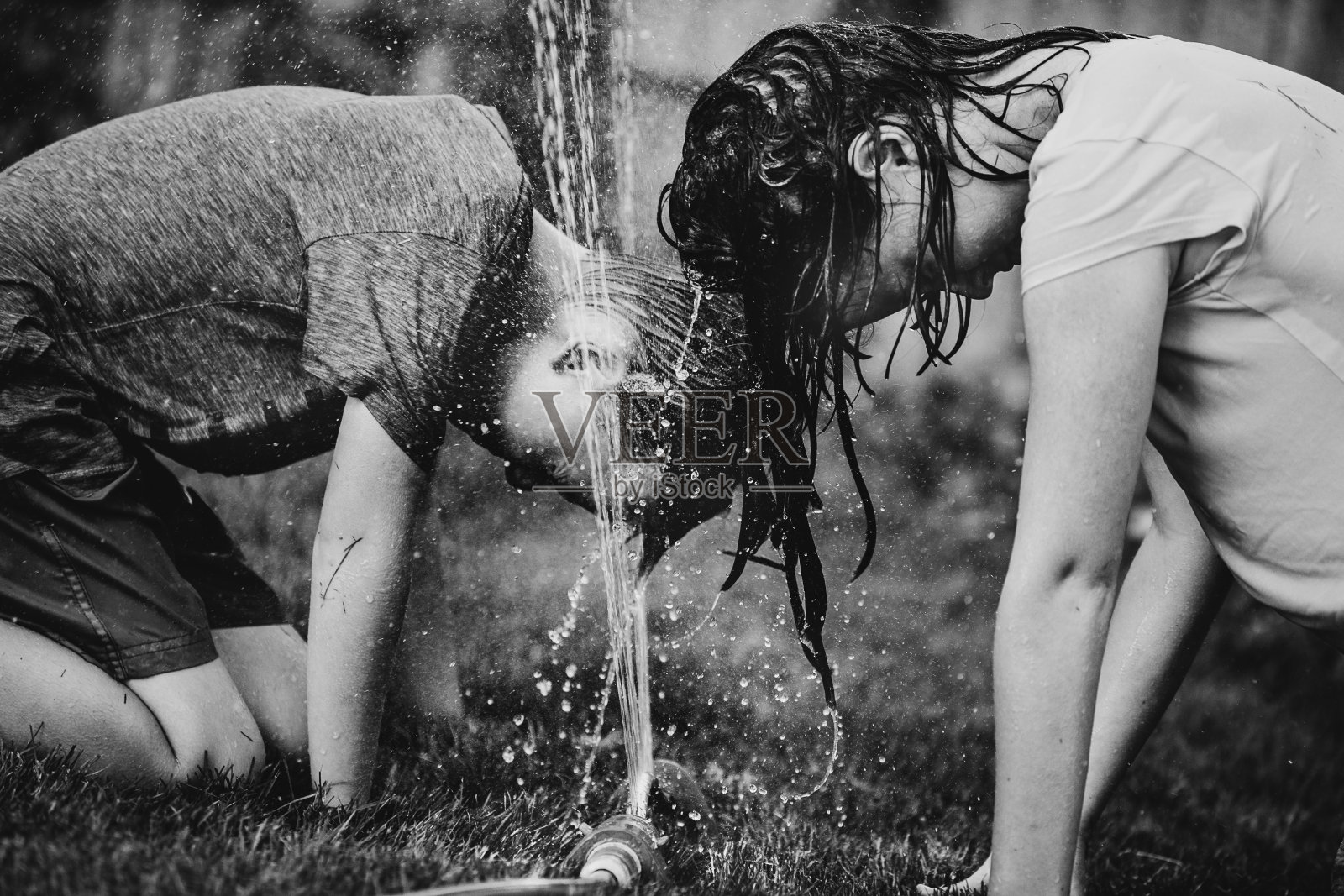 小男孩和小女孩在玩花园里的洒水器。照片摄影图片