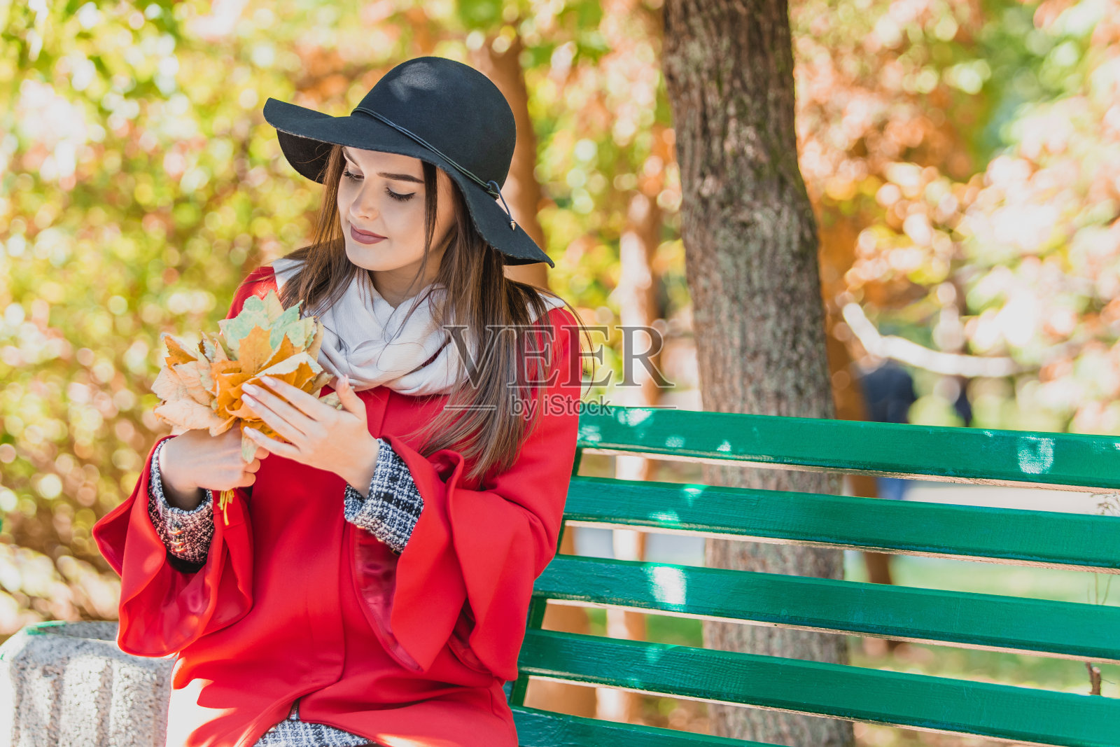 浪漫的女孩坐在公园的长椅上，抚摸着黄色的秋叶，梦想着愉快的面部表情。照片摄影图片