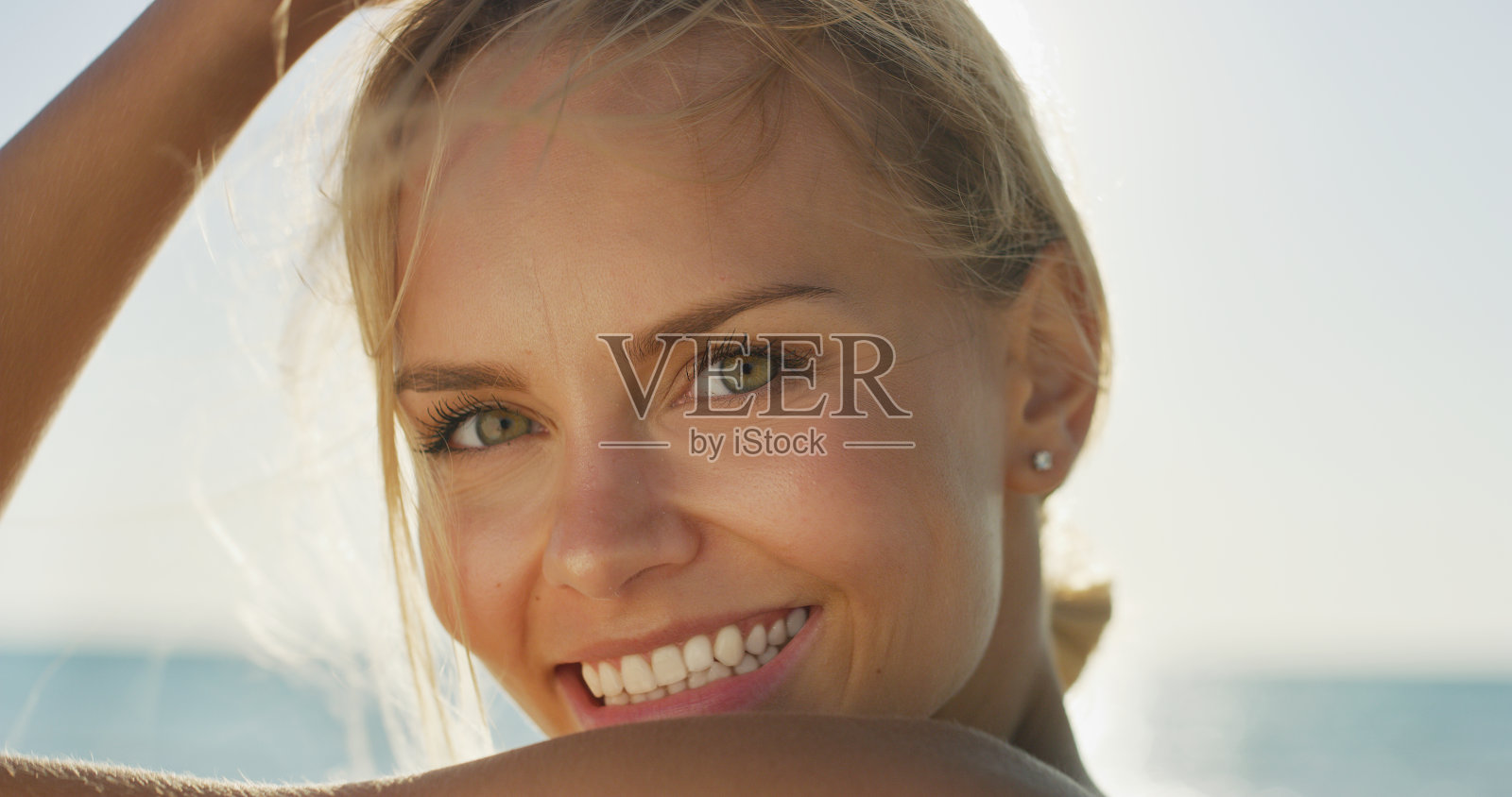 年轻的微笑女孩的肖像是快乐的享受在一个阳光明媚的日子在海边的海边度假。照片摄影图片