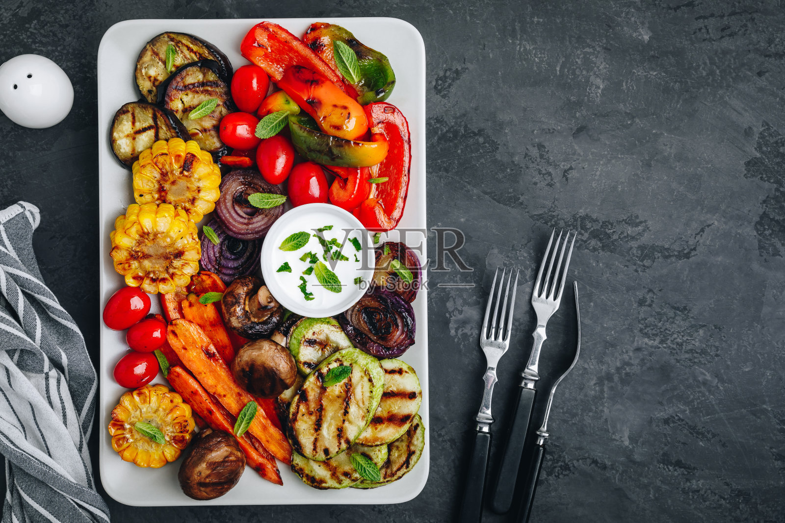 烤蔬菜拼盘与西葫芦，蘑菇，茄子，胡萝卜，胡椒钟，番茄，洋葱，玉米，和酸奶薄荷酱照片摄影图片