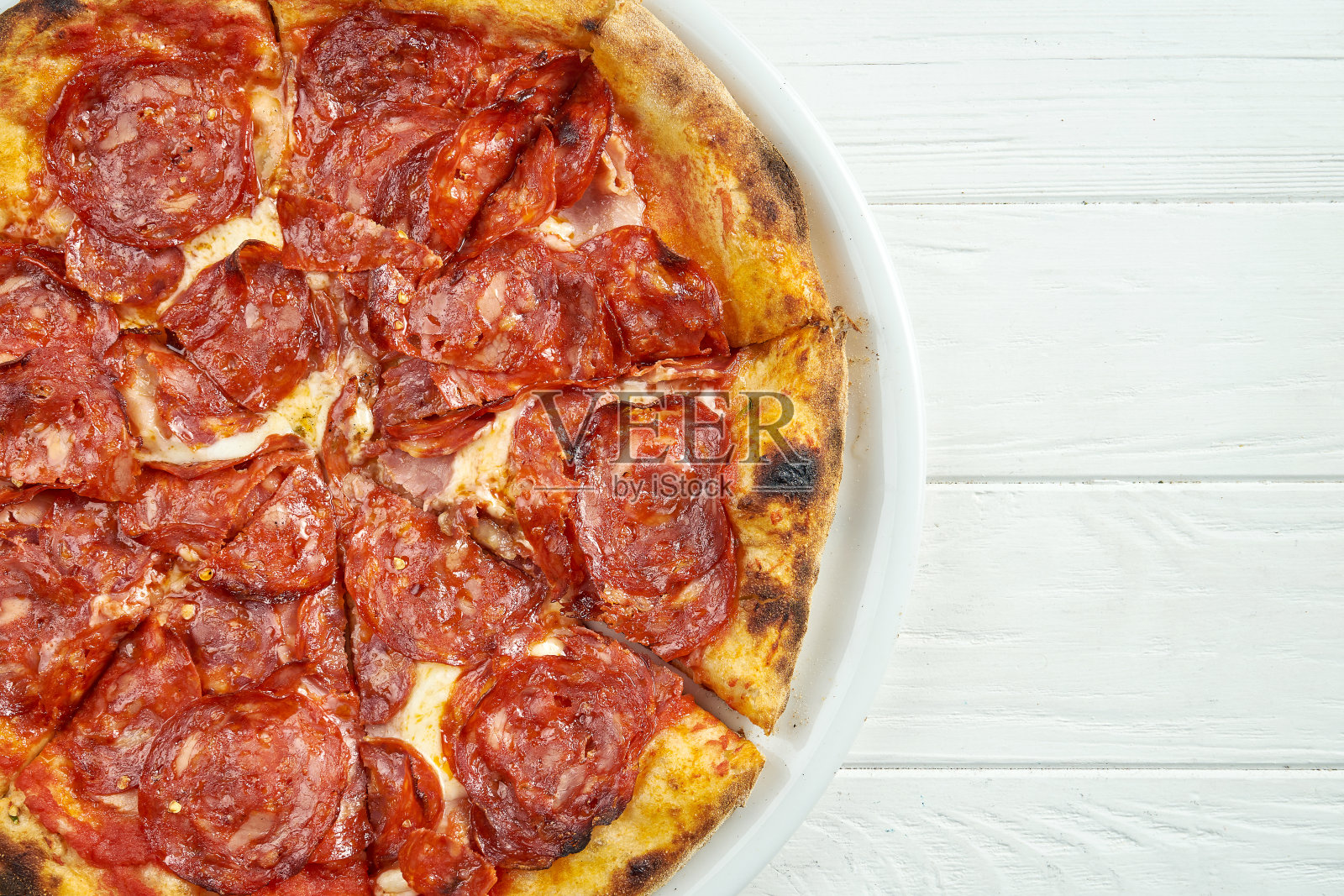 开胃的自制披萨与香肠腊肠和融化的奶酪在白色的盘子上，在白色的木制背景照片摄影图片