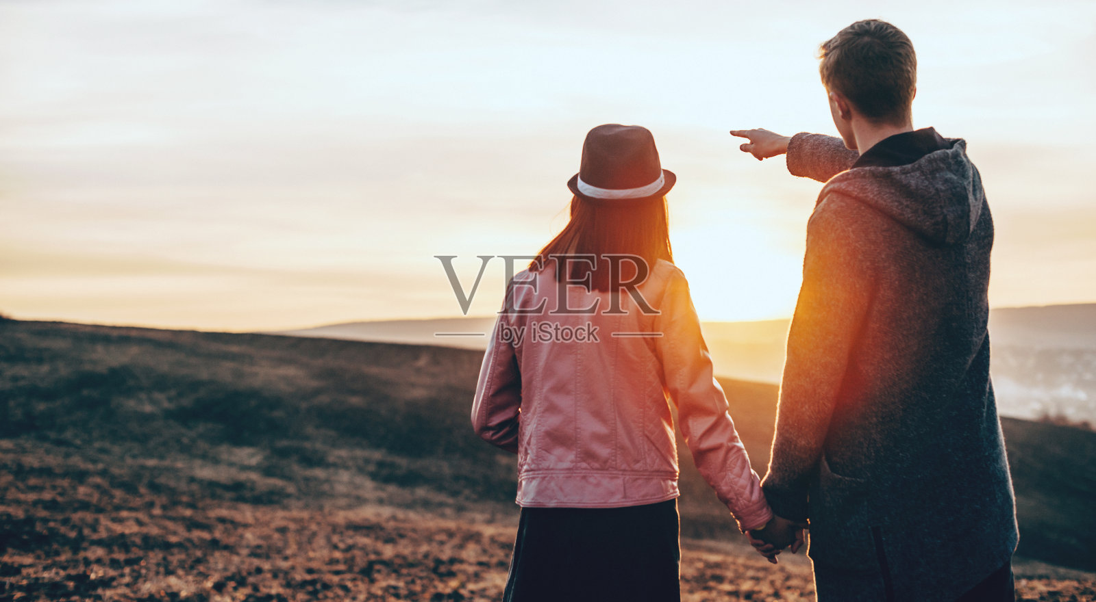 一个白人男人和他的女人手牵着手走在田野里，指着风景照片摄影图片