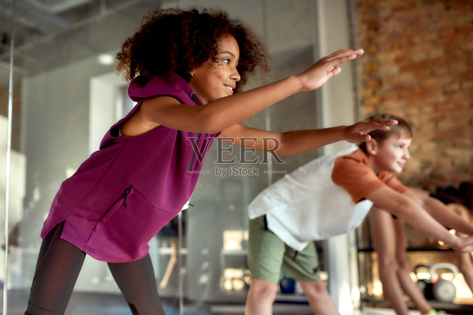 加入我们的行列。一个女孩正在热身，和其他孩子一起在健身房锻炼。运动，健康的生活方式，积极的童年观念照片摄影图片
