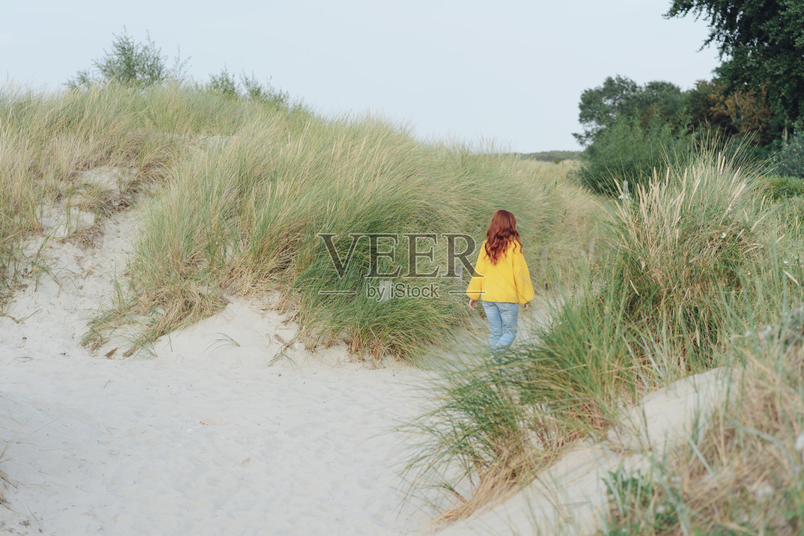 一名年轻女子正穿过海岸的沙丘照片摄影图片