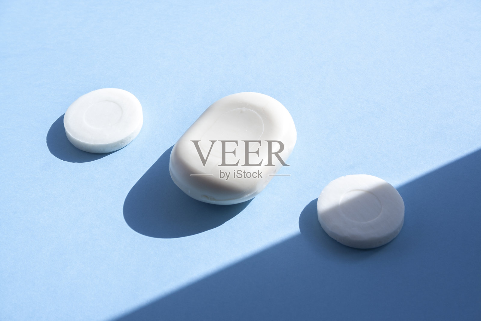 三个肥皂侧面的蓝色背景与时尚的照明从太阳。洗你的手。肥皂防细菌和病毒。遵守卫生和无菌，抗击冠状病毒。照片摄影图片