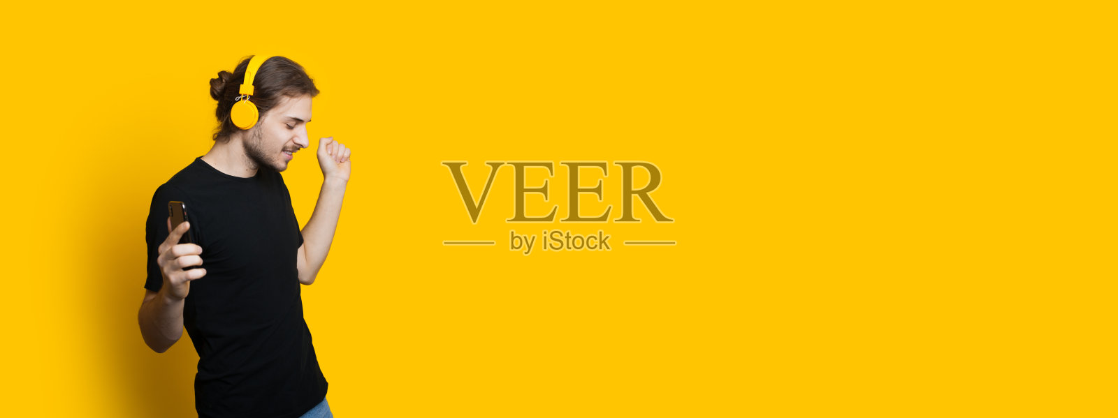 英俊的白种人长头发和胡子正在通过耳机听音乐，而摆姿势附近的黄色自由空间照片摄影图片