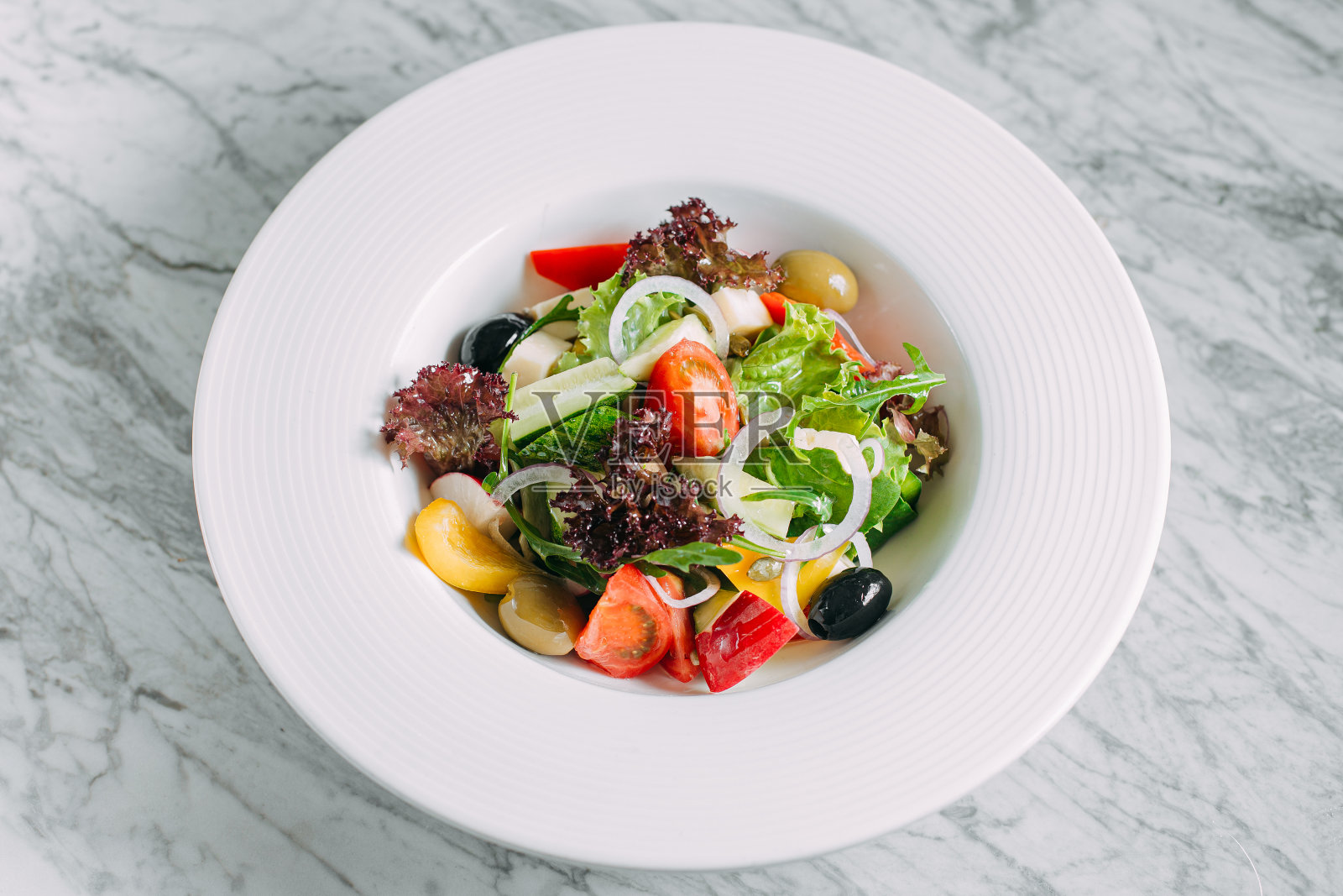 素菜西红柿、橄榄、胡椒沙拉在白色盘子里放在大理石桌子上，是健康的食物照片摄影图片