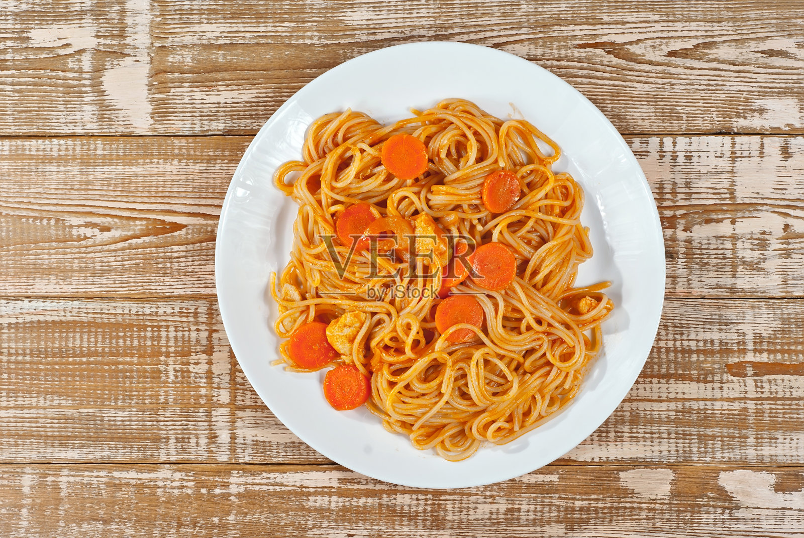 木桌上的白盘子里放着胡萝卜意大利面。粉条配橙汁放在破旧的粉色板上。将文字放置在板块附近。复制空间设计。照片摄影图片