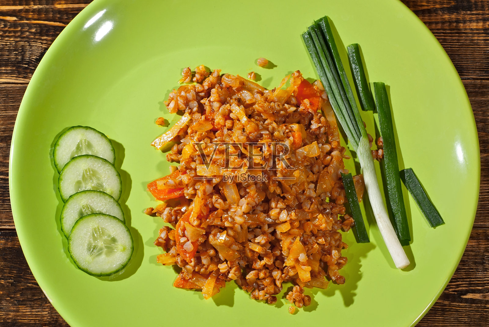 木桌上的绿盘子里装着荞麦、黄瓜、欧芹和洋葱。食物在餐具的背景，破旧的旧板。照片摄影图片