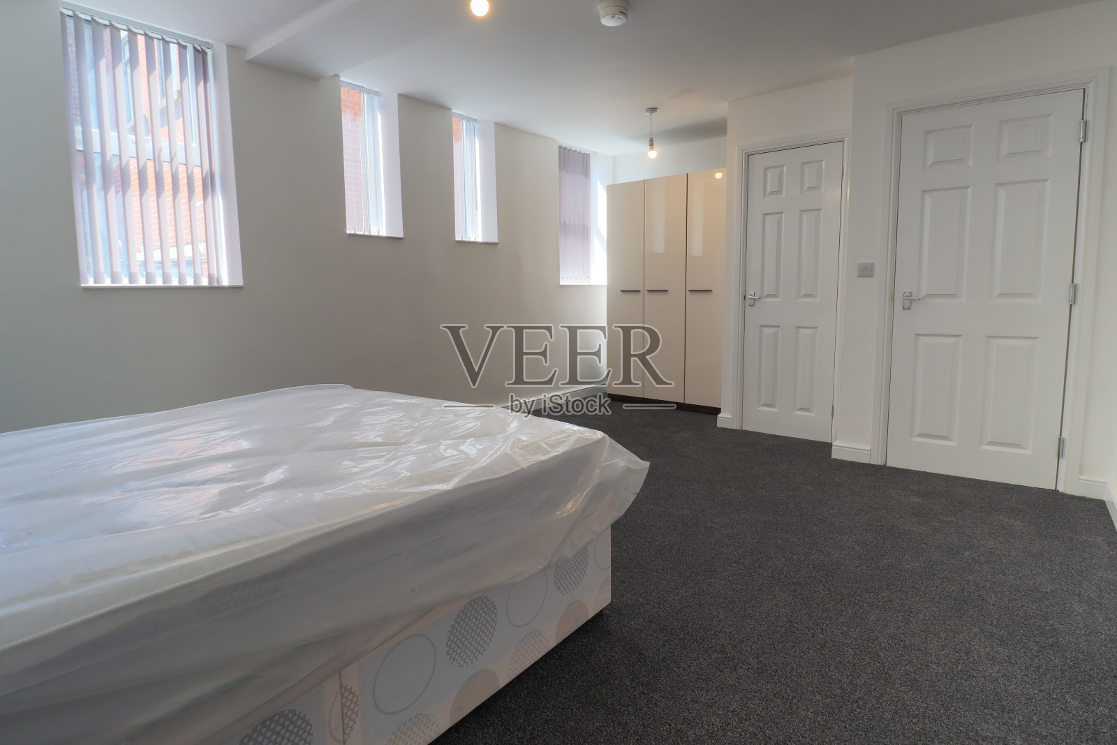 一间新装修的典型英式卧室，有一张大床和衣柜，白色的墙壁，灰色的地毯和百叶窗。照片摄影图片