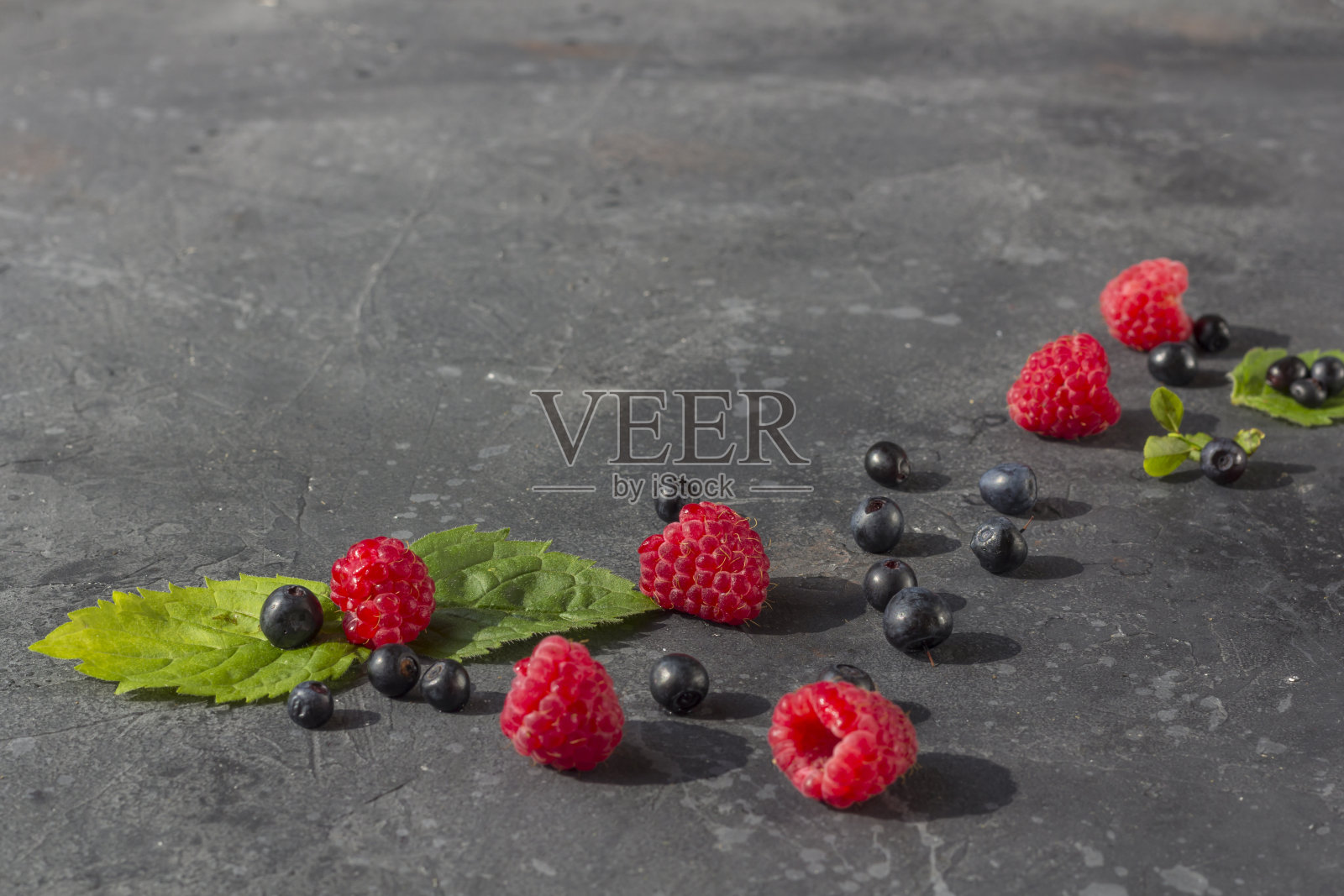 新鲜多汁的树莓和蓝莓与薄荷叶在黑暗的背景。夏天的浆果在黑色。健康，素食，饮食，节食。平铺，复制空间的文本。照片摄影图片