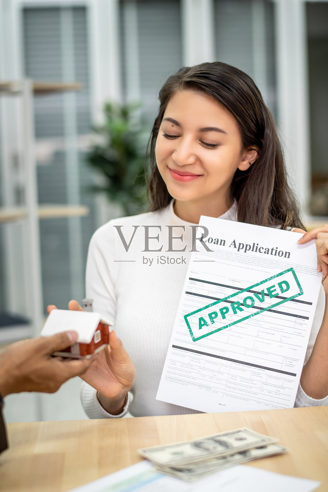 年轻有魅力的亚洲女性持有贷款协议文件，对银行感到满意，批准贷款购买她的房子。客户购买房地产的概念。照片摄影图片