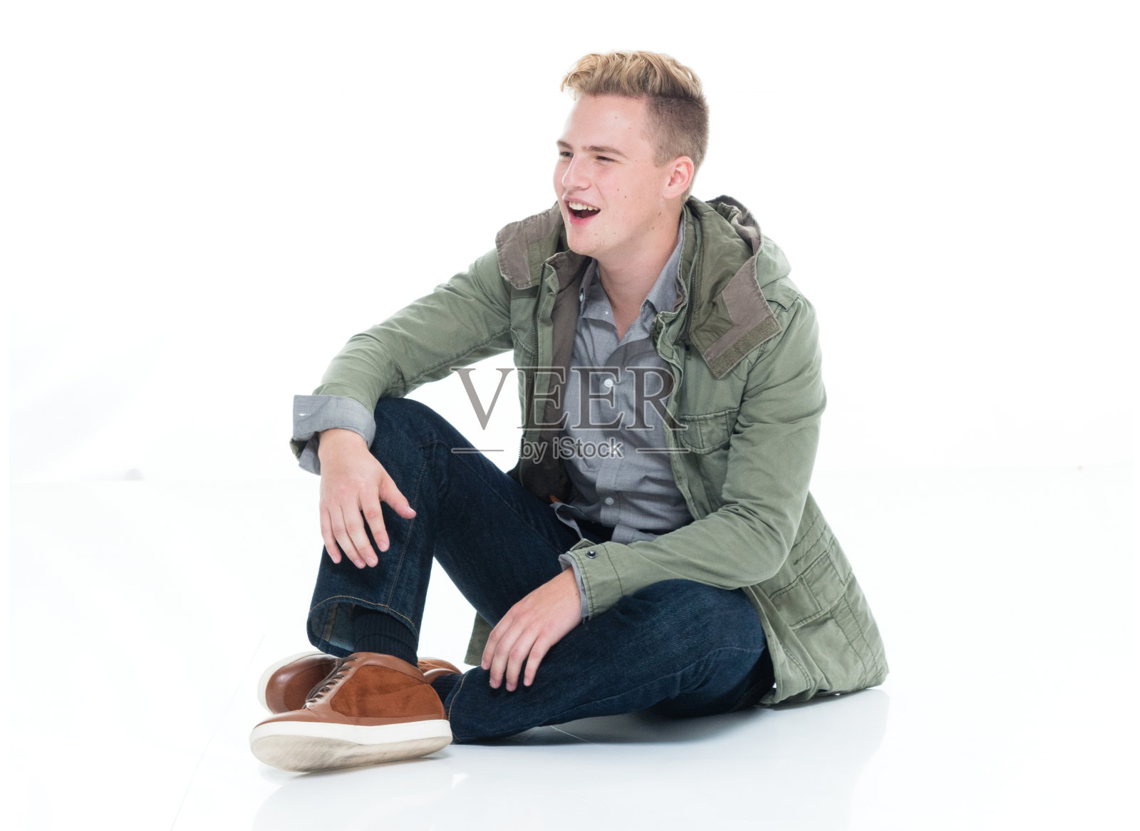 白人年轻男子坐在地板上，穿着夹克在白色背景照片摄影图片