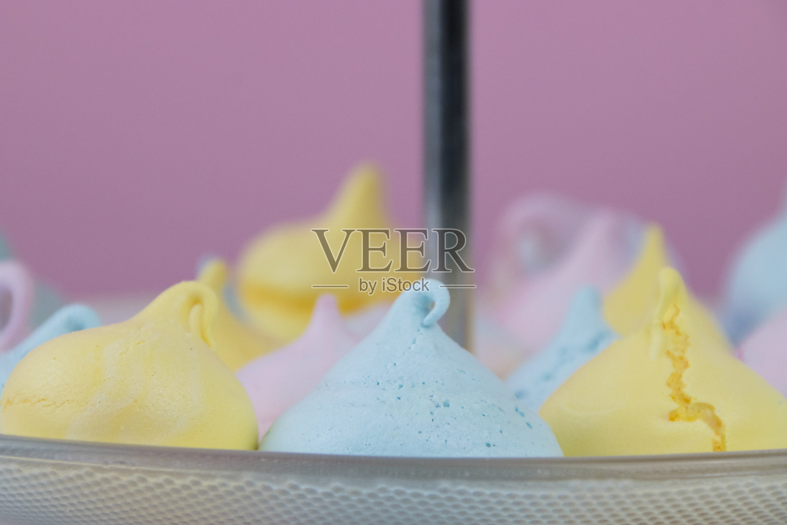 玻璃盘子上的蓝色蛋白酥皮被粉色、黄色和蓝色蛋白酥皮所包围。甜的零食的概念照片摄影图片