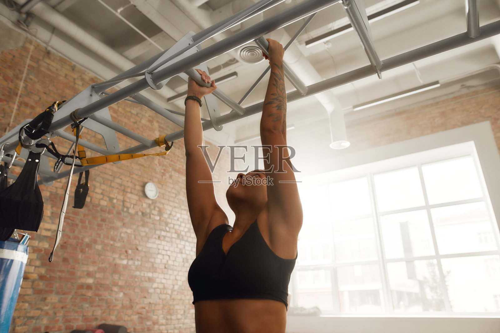 现在就培养你的身体。在工业健身房的酒吧里做引体向上的运动女人照片摄影图片