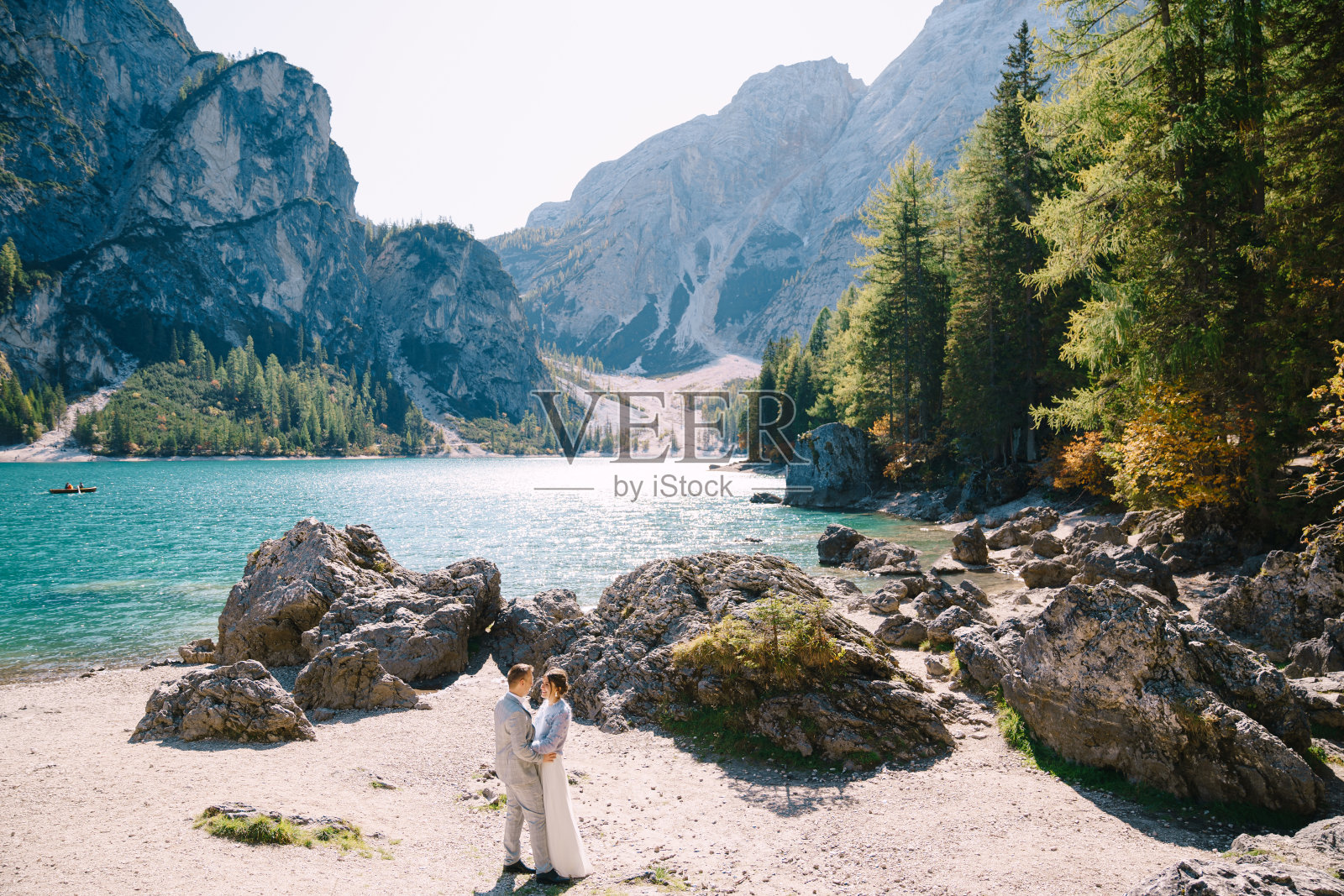 在意大利，新娘和新郎站在石头的背景下俯瞰布雷斯湖。在欧洲的Braies湖上举行旅游婚礼。相爱的新婚夫妇走在令人惊叹的自然背景下。照片摄影图片