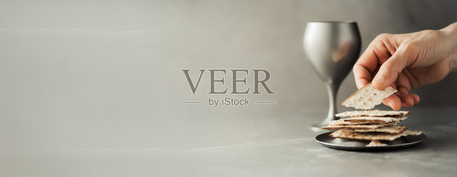 手持圣餐杯和酵母饼，灰色背景上的木制十字架。基督教圣餐，纪念耶稣的牺牲。复活节逾越节。圣体圣事概念。基督教的象征和信仰照片摄影图片