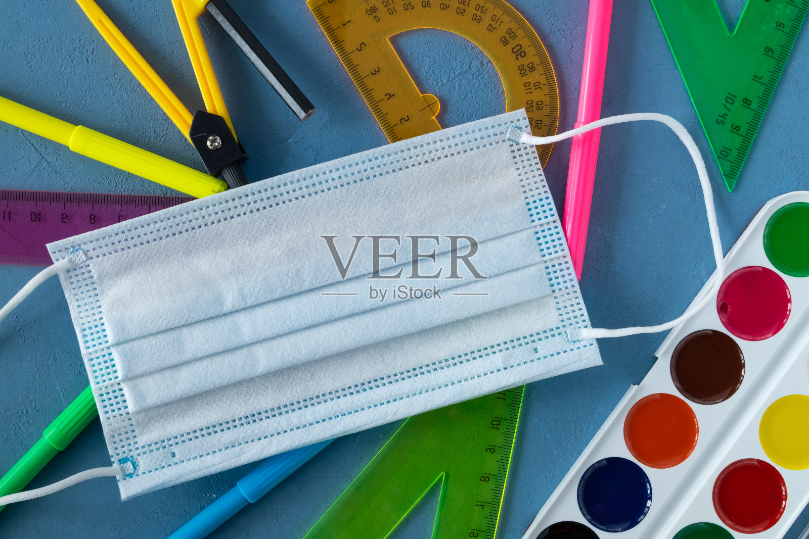 蓝色背景的学校用品和医用口罩。照片摄影图片