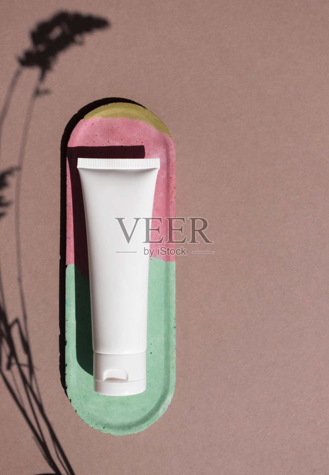 模型白色塑料容器化妆品在棕色背景与时尚的草药阴影和复制空间俯视图，上面。Tube for cream, moisturizer, lotion, facial cleanser on colorful concrete decor plate彩绘混凝土装饰板照片摄影图片