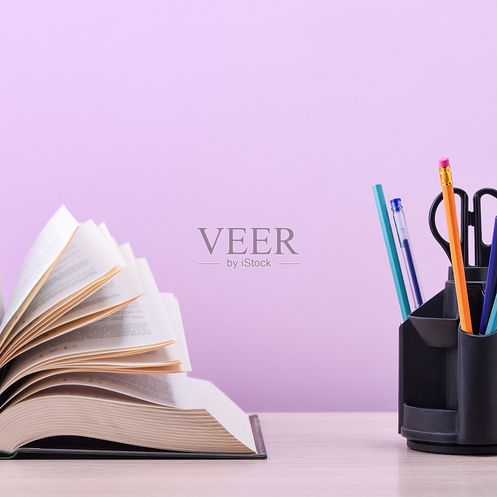 那是一本厚厚的大书，书页像一把扇子一样摊开，在淡紫色的背景上，有一个架子，上面放着钢笔、铅笔和剪刀。照片摄影图片