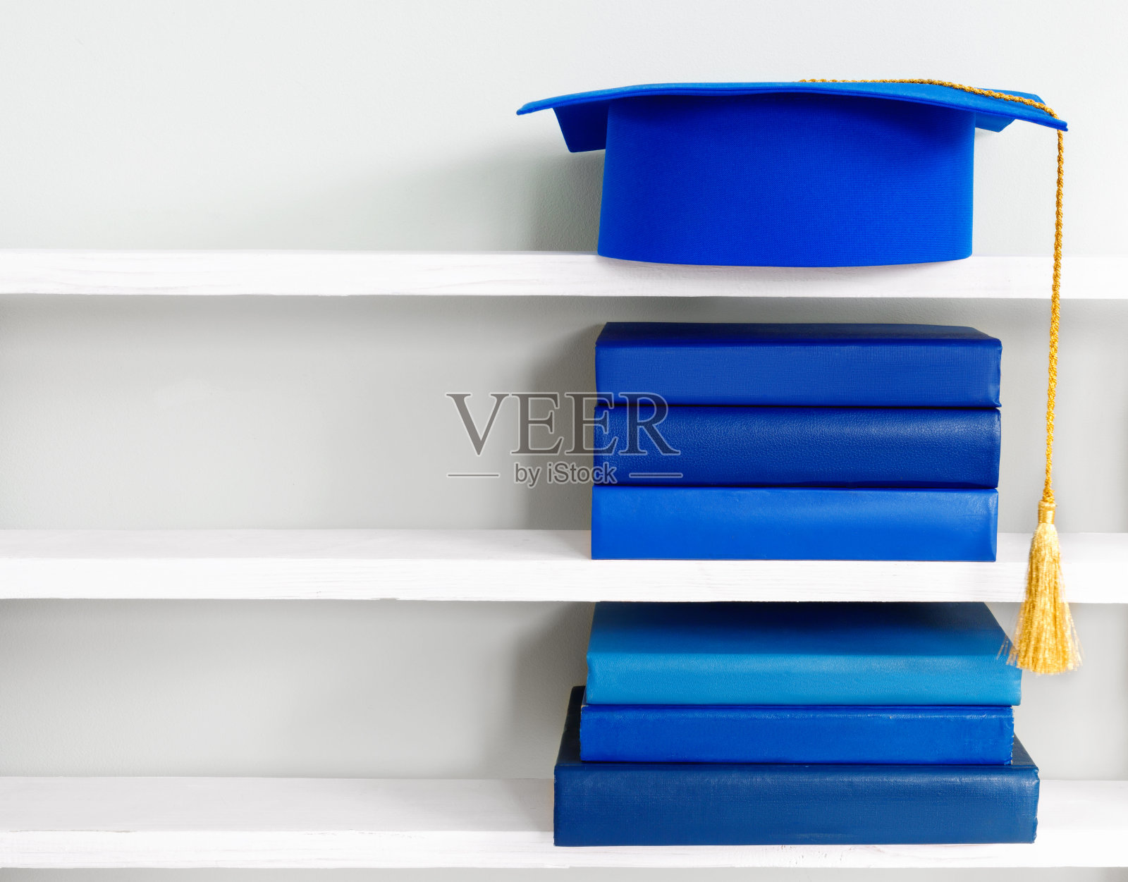 蓝色的毕业帽放在书架上的一堆书上照片摄影图片