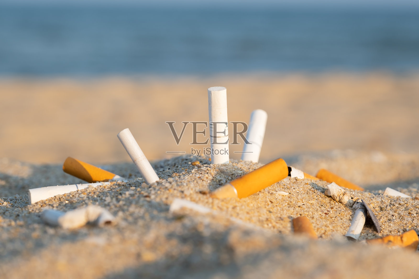 海边沙滩上的黄沙上的烟头，映衬着蓝天和大海。人性的问题。吸烟，坏习惯。尼古丁上瘾。垃圾照片摄影图片
