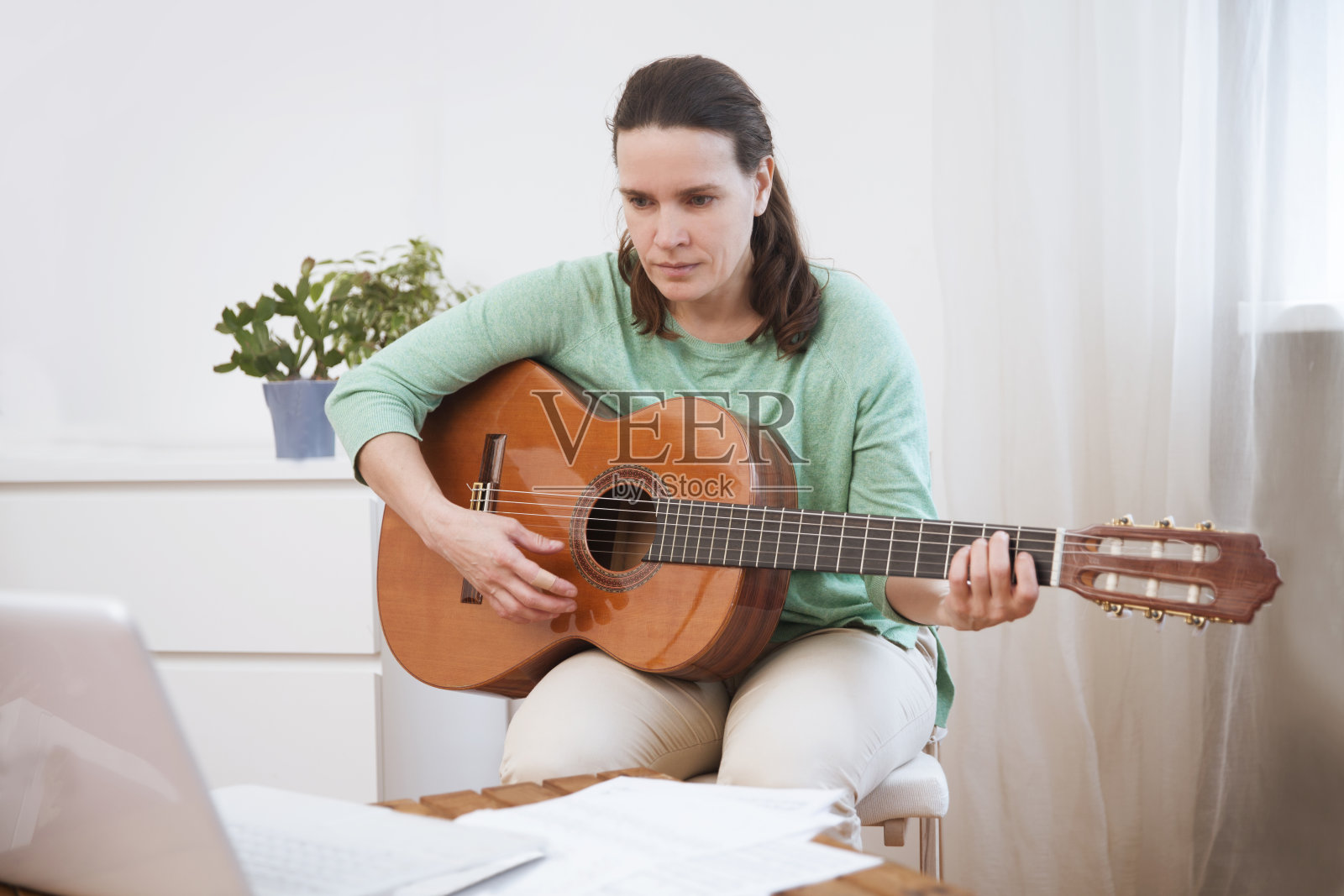 在家里练习的时候，她会弹原声吉他，在笔记本电脑上看在线课程。呆在家里。隔离。在线培训，在线课程。照片摄影图片