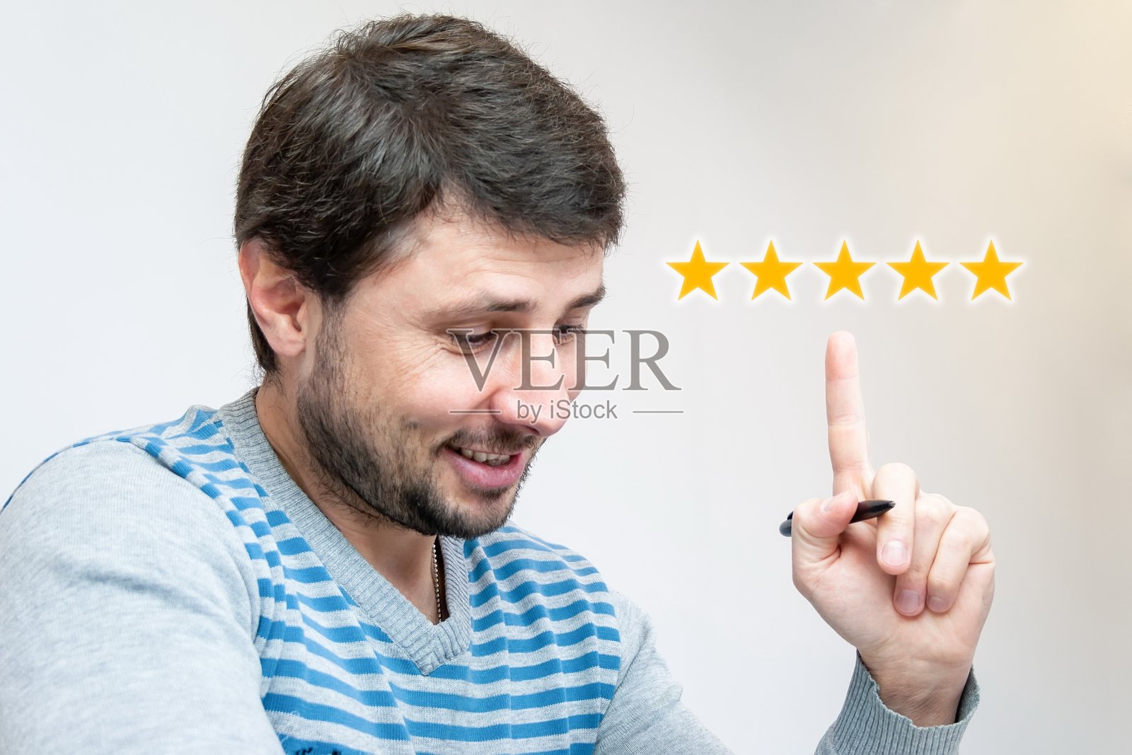 英俊的微笑的胡子男子，手里拿着一支笔，食指向上指着五颗明亮的橙色星星。客户对在线商店中的产品或应用程序给予最高的评价照片摄影图片