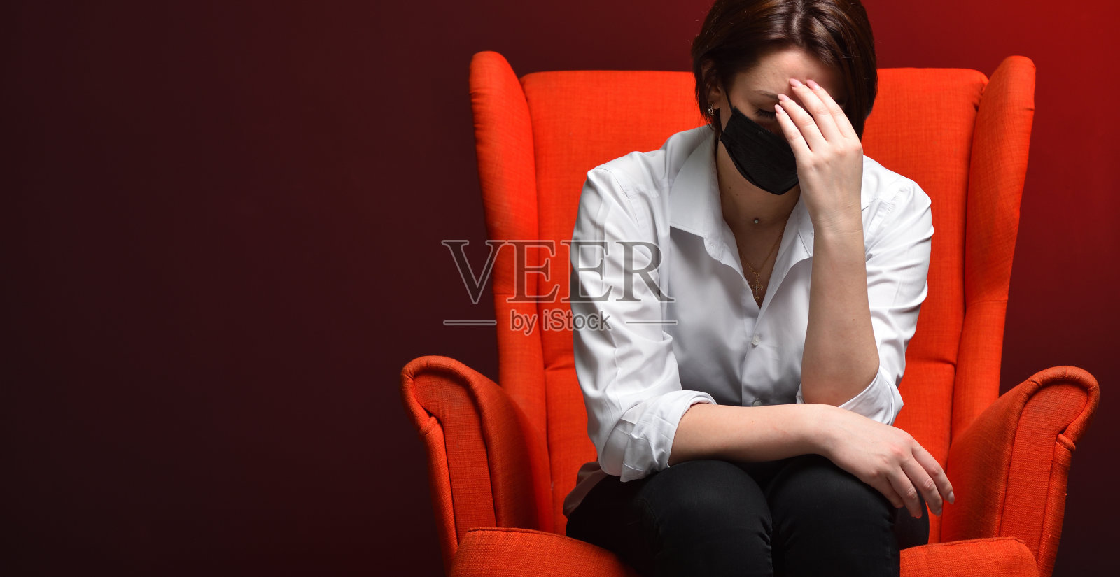 在一次测试和一场冠状病毒大流行期间，一名紧张的妇女坐在一张红色椅子上抱着头。病毒式危险和恐惧的概念照片摄影图片