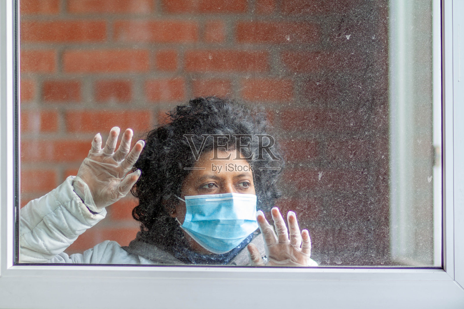 一名妇女在隔离期间戴着防护口罩向窗外张望照片摄影图片