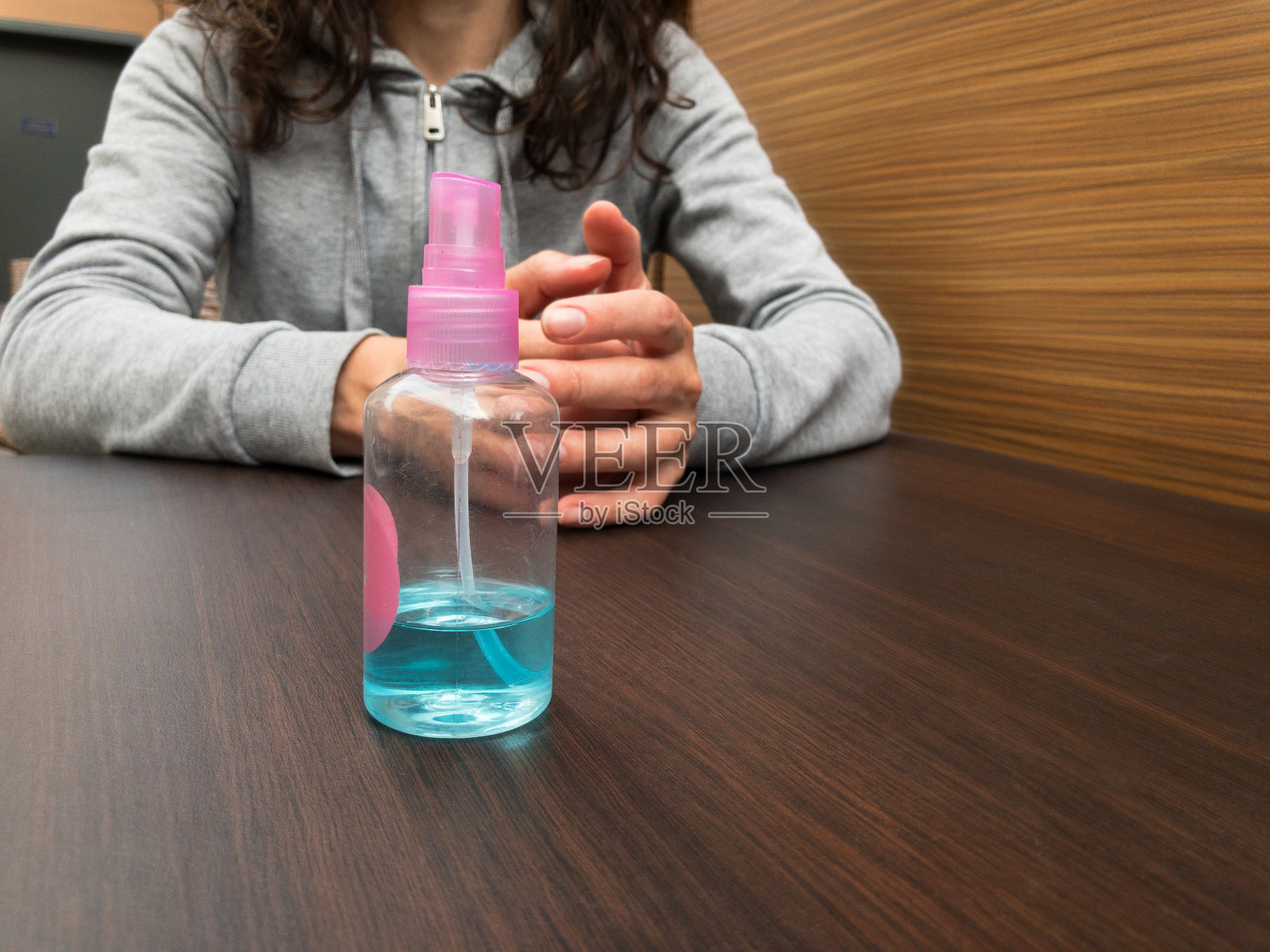 在一家街头咖啡馆的夏日露台上，一个等待点餐的女孩面前放着一个手动消毒液。减轻检疫措施。照片摄影图片