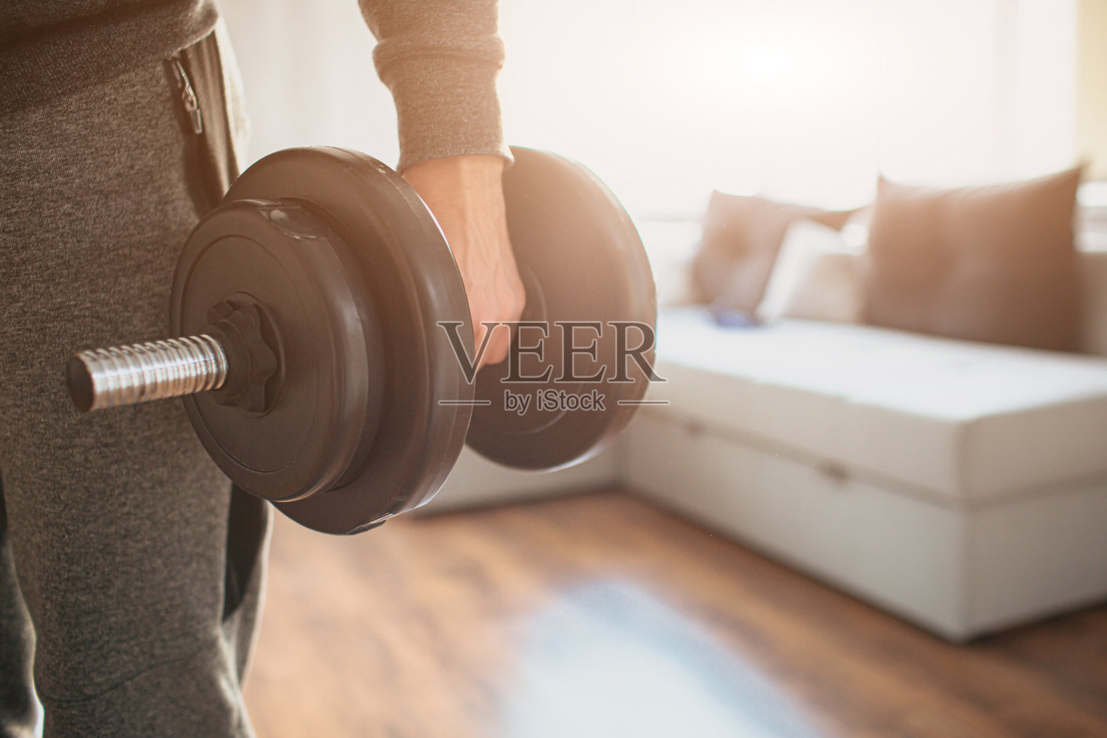 年轻的普通人在家里从事体育运动。截屏:木工初学者站在地板上，手里拿着哑铃。准备开始他的第一次训练了。普通人努力改善自己的身体。照片摄影图片