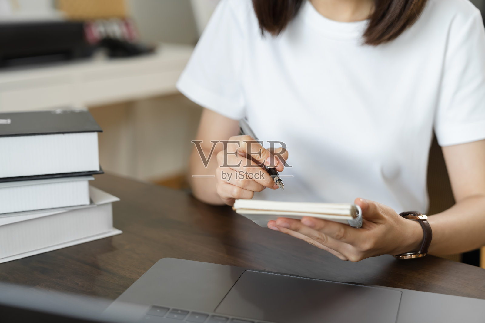 女人手拿书和笔与笔记文本学习在笔记本电脑在家里。照片摄影图片