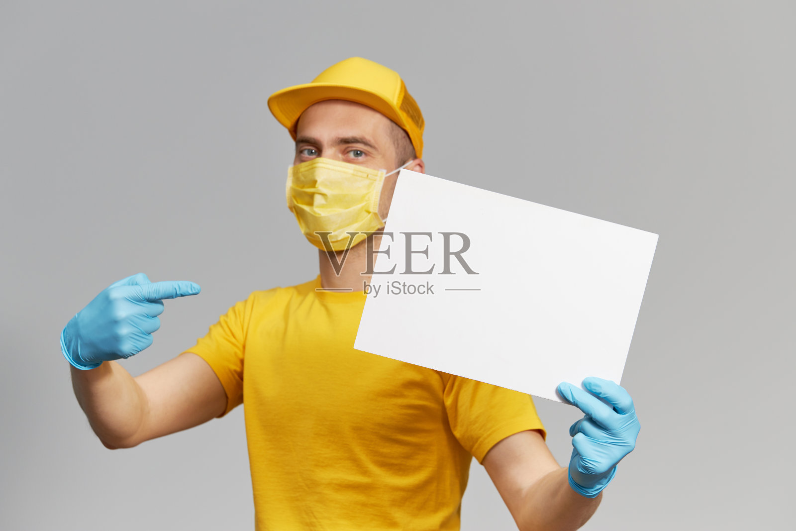 黄色制服的快递员，戴着防护口罩和手套送外卖和咖啡。交付服务处于隔离状态。举着白色的文字标志照片摄影图片