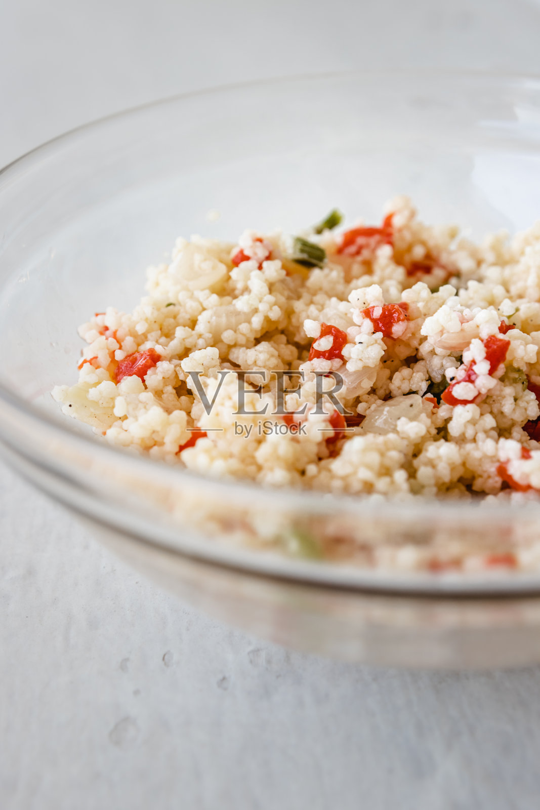 手里拿着一个盛着蒸粗麦粉沙拉的玻璃碗。照片摄影图片