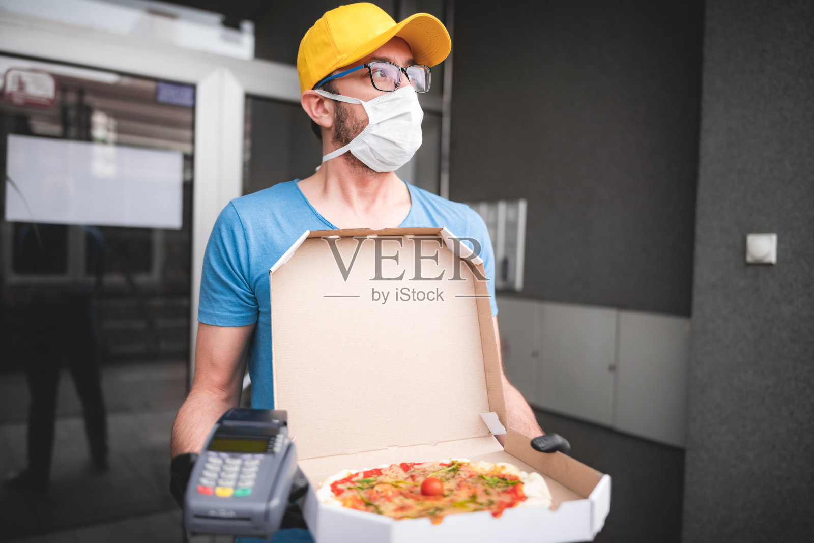 送餐员带着医用防护口罩拿着披萨盒-病毒和大流行的日子，送餐上门。照片摄影图片
