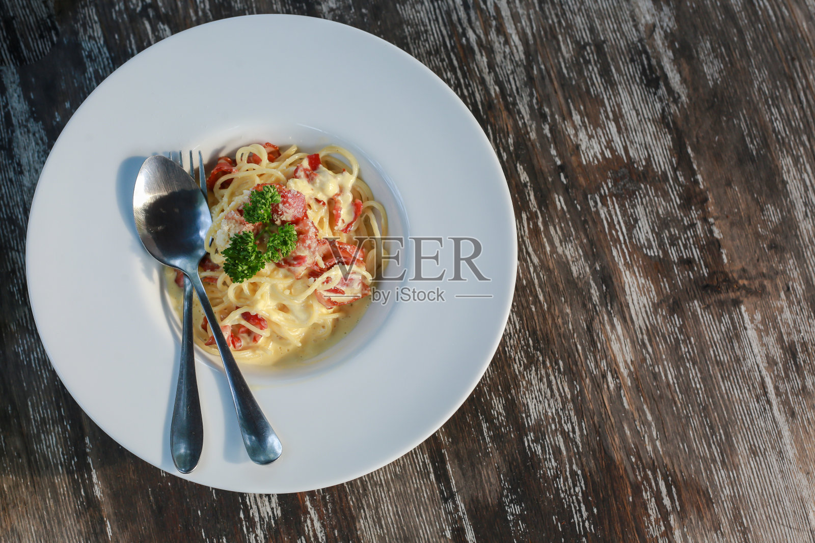 意大利面条，美味，容易做泰式，顶部用欧芹蔬菜装饰。放在一个白色的盘子上，旁边放着一把勺子和叉子，放在一张旧的木桌上照片摄影图片