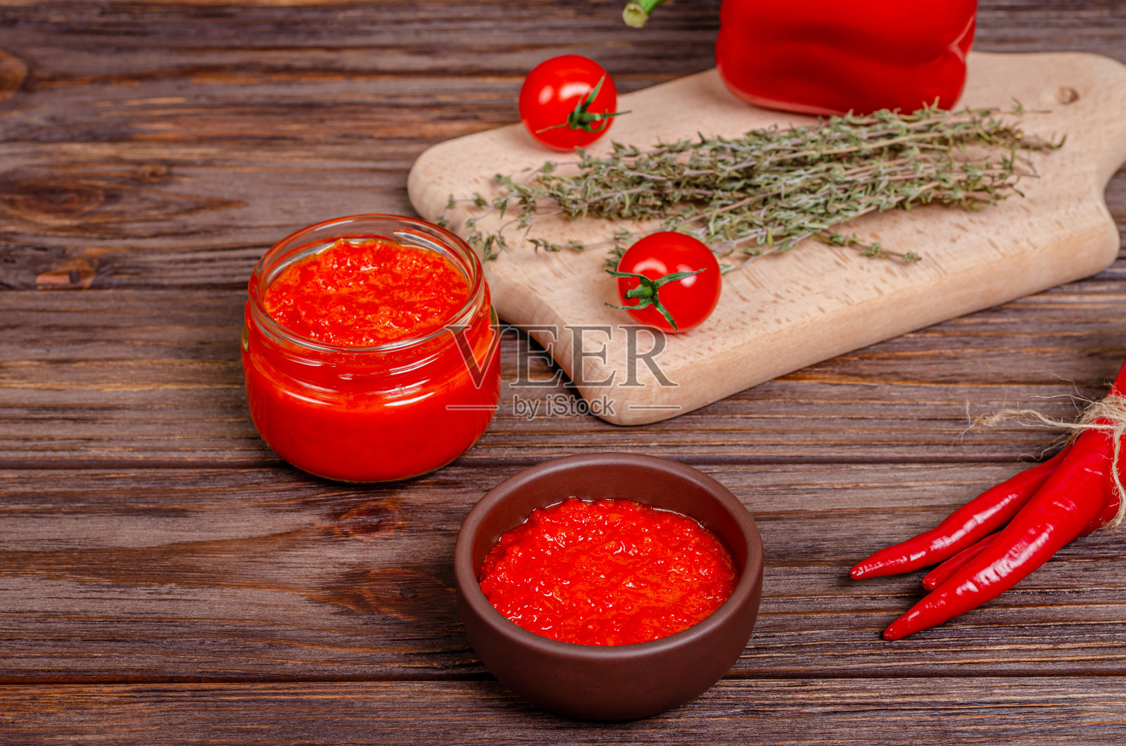 Ajvar或pinjur红蔬菜酱或辣椒和番茄慕斯放在一个陶土碗和一个玻璃罐子里，放在质朴的木桌上照片摄影图片