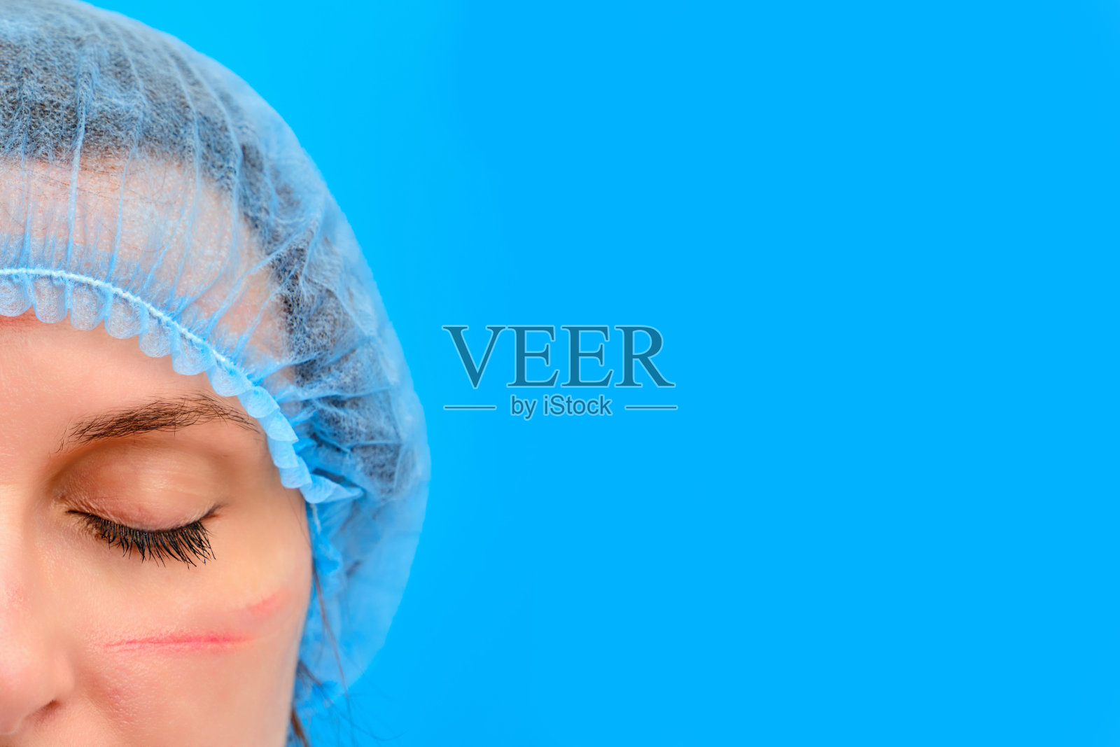 戴着蓝色医疗贝雷帽戴着口罩，有伤口的医生，有文字拷贝空间。一个护士在蓝色背景上，脸上有防护服的痕迹，特写。抗击新冠肺炎大流行的理念。照片摄影图片