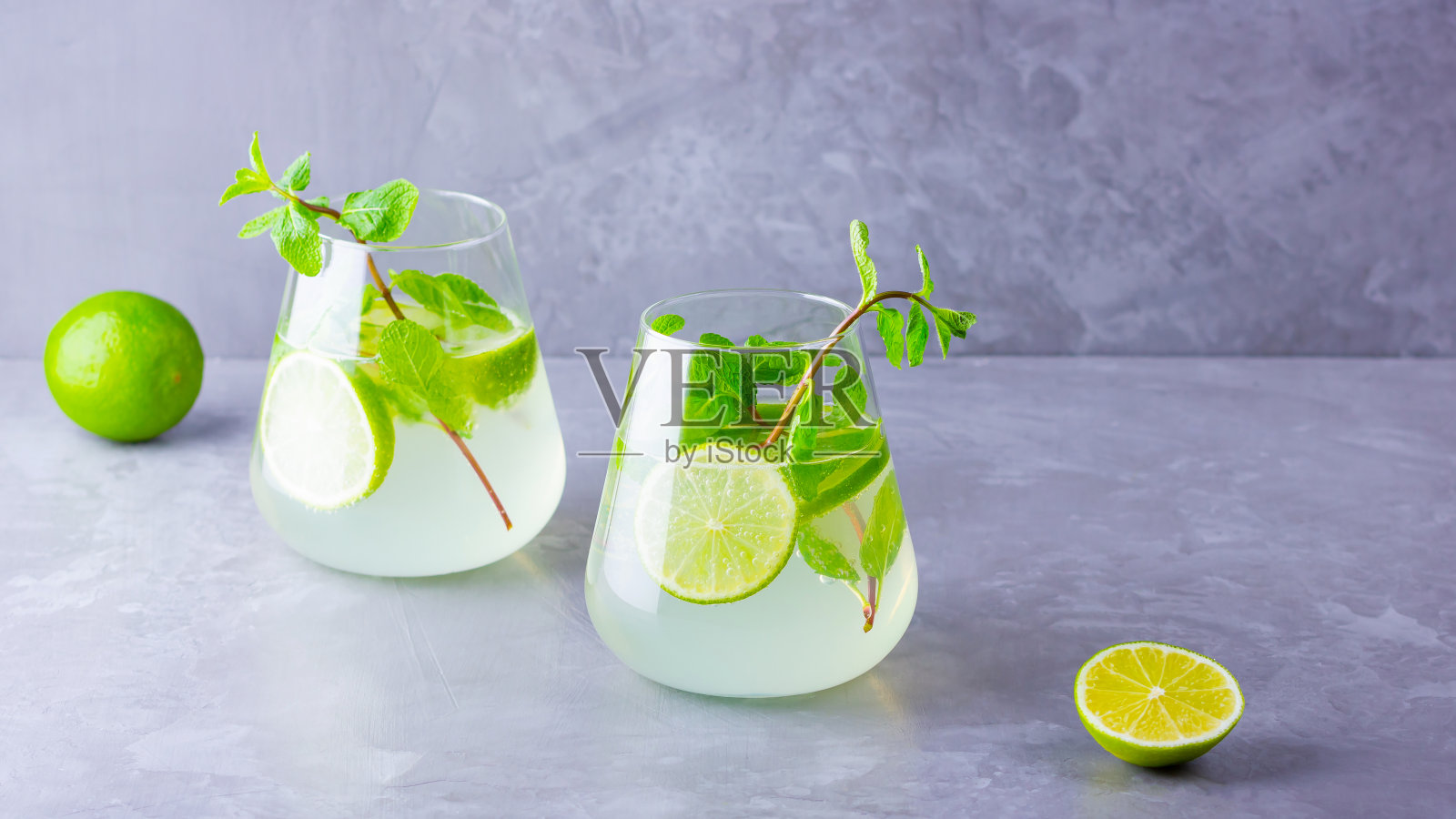 莫吉托鸡尾酒，柠檬和薄荷杯。灰色背景下的两杯莫吉托。清新的薄荷鸡尾酒加酸橙。注入水照片摄影图片