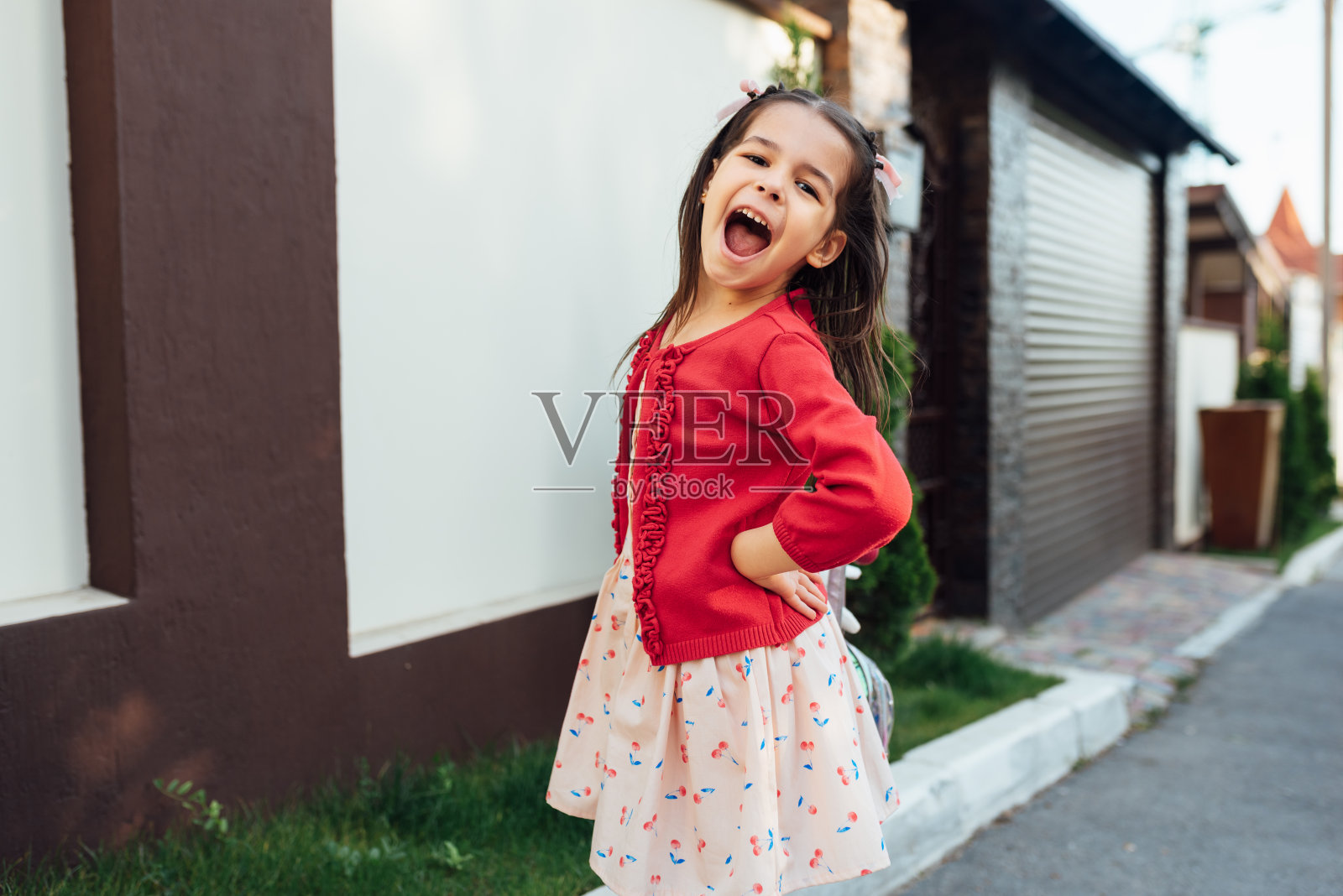 可爱的小女孩在放学回家的时候笑着站在她家附近。微笑的孩子在户外玩耍，有着快乐的表情。快乐的孩子微笑着，在户外摆姿势照片摄影图片