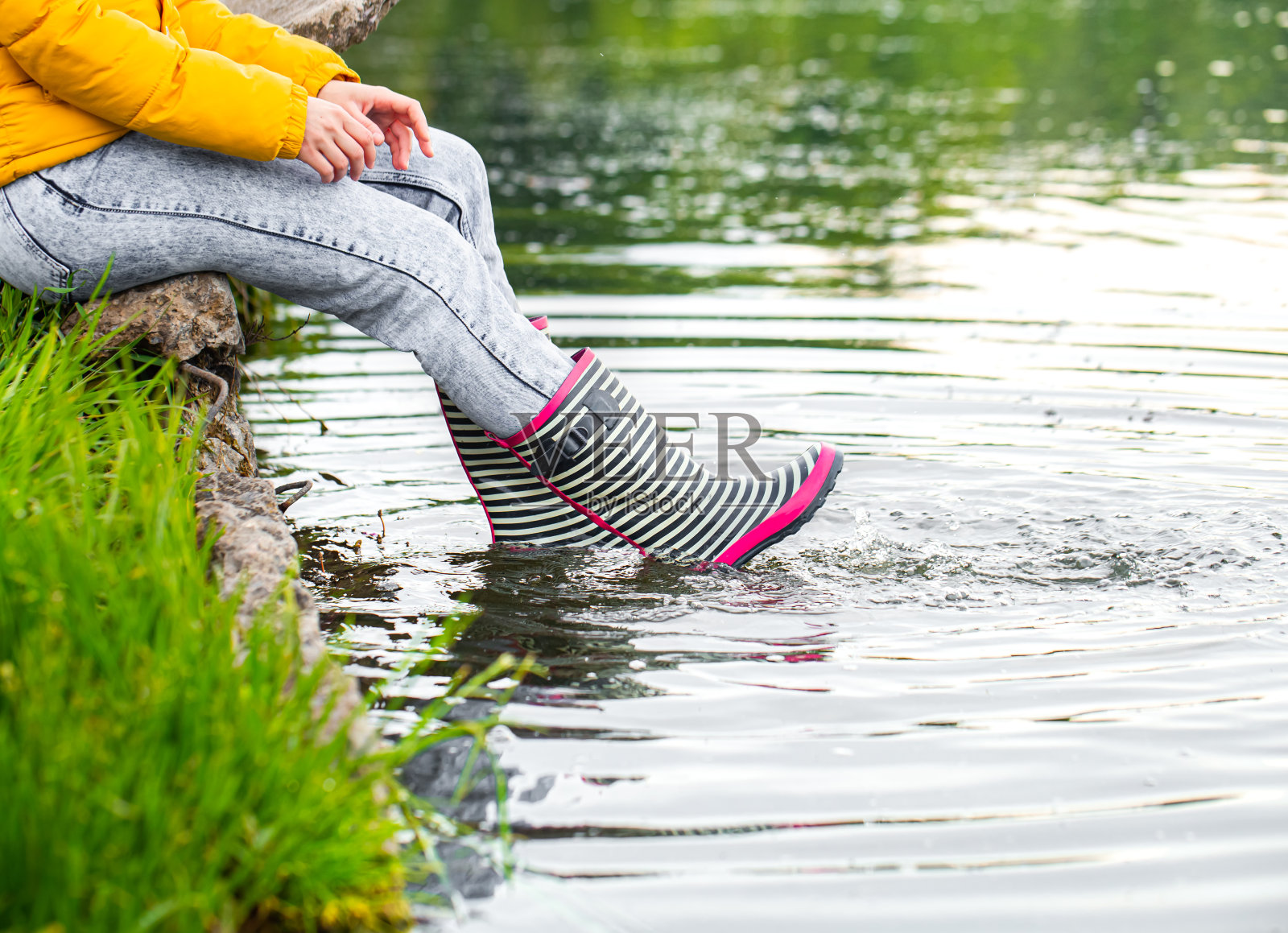 一个年轻女子穿着胶靴坐在湖边。照片摄影图片