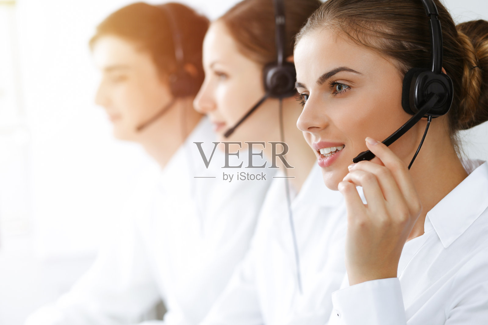 呼叫中心。美丽的年轻女子使用耳机和电脑帮助客户在阳光明媚的办公室。经营理念照片摄影图片