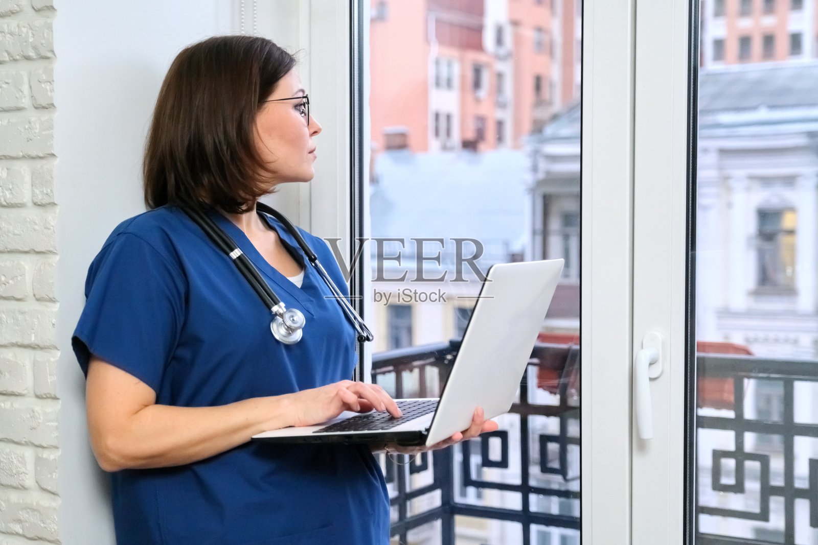 女护士使用笔记本电脑，医生在医务室窗户附近照片摄影图片