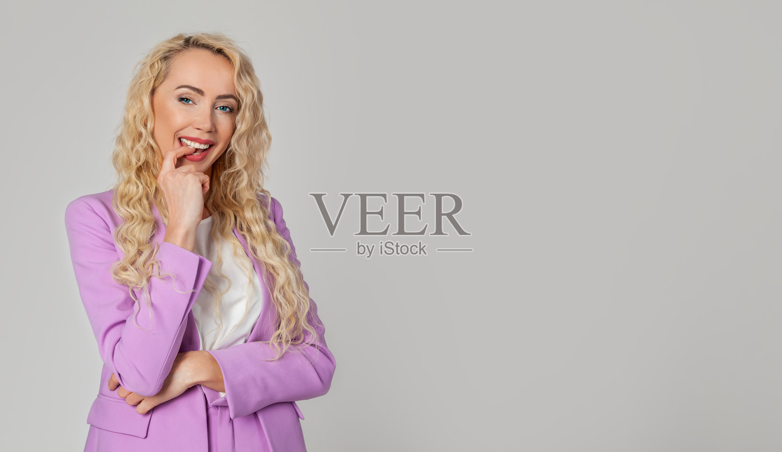 迷人迷人的金发碧眼女人愉快地咬她的手指，满足地微笑，快乐地微笑照片摄影图片