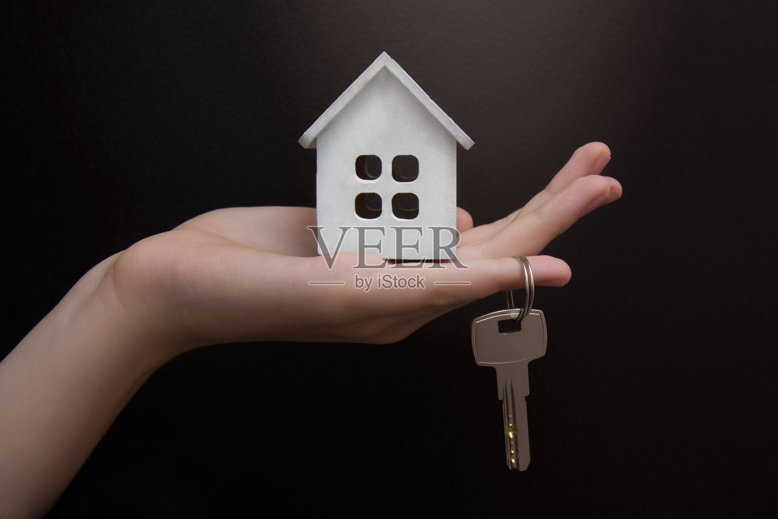 手握钥匙的特写，黑色背景上的白色木屋模型。Copyspace照片摄影图片