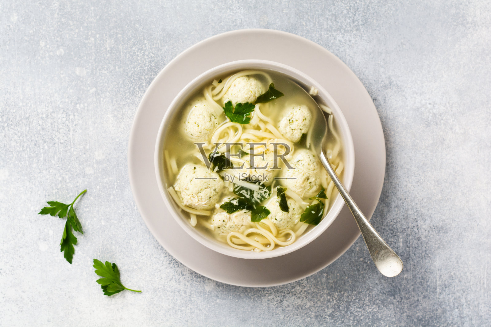 灰色背景的桌子上，用陶瓷碗盛着鸡肉丸、蛋糊、帕尔玛干酪和欧芹汤。传统的意大利肉汤。前视图。照片摄影图片