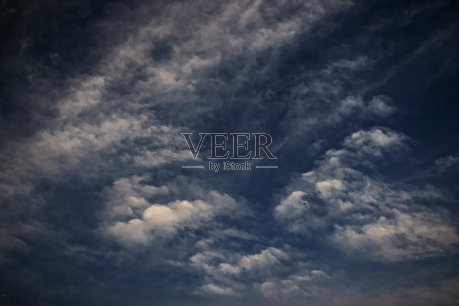 深蓝色的天空下散布着一层薄薄的白云。照片摄影图片