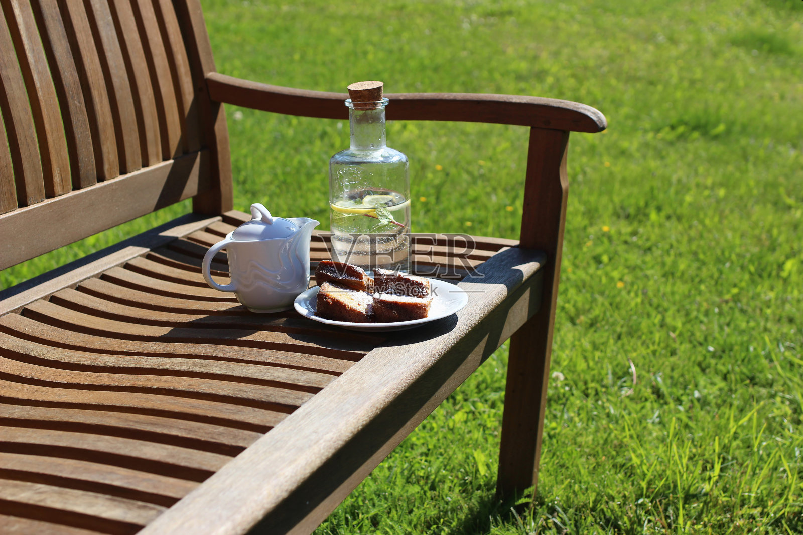 木凳上放着咖啡壶、玻璃瓶自制的柠檬水和蛋糕，模糊了绿草的背景。户外休息时间。野餐，游园会小吃，放松概念。没有人。照片摄影图片
