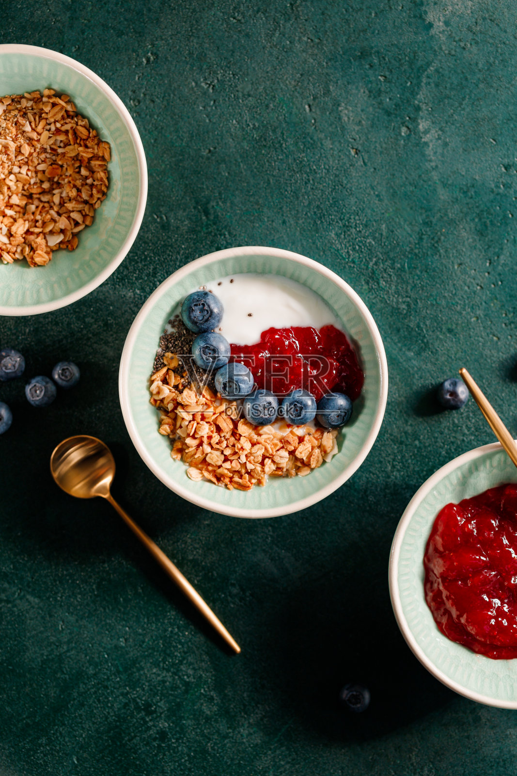 俯视图早餐麦片，酸奶，草莓酱，奇亚籽和蓝莓在一个深绿色的桌子上。照片摄影图片